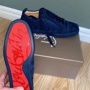 Marinblå mocka skor från Christian Louboutin - Säljer ett par mörkblå sneakers i mocka från Christian Louboutin med ikonisk röd sula och broderad logga på hälen. Skorna har snörning och rund tå, och kommer med originalpåse och tillbehör.