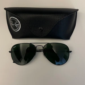 Ray-Ban - Klassiska svarta aviator-solglasögon från Ray-Ban med mörkgröna glas och tunn metallbåge. Kommer med originalfodral i svart. Perfekt accessoar för en cool och tidlös stil. ALDRIG ANVÄNDA. Nypris 1200kr
