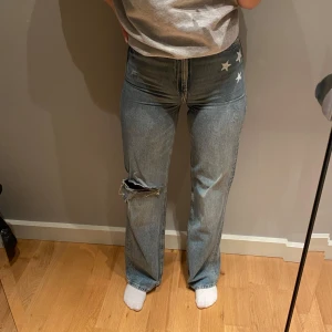 Blå jeans med stjärndetaljer - Blå jeans med raka ben och vita stjärnor på ena höften som jag själv målat, Jeansen har en slitning på ena knät
