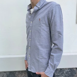 Polo Ralph Lauren skjorta - Säljer en grå skjorta från Ralph Lauren i slim fit-modell. Skjortan har långa ärmar, klassisk krage och knappar framtill. Broderad logga på bröstet. Perfekt för en stilren look. Denna är i fint skick. Nypris är 2149. Hör av er vid några frågor 