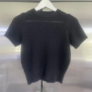 Svart stickad topp med hålmönster - Säljer en svart stickad topp med korta ärmar och rund hals. Tröjan har ett genomgående hålmönster som ger en luftig känsla och bred ribbad kant nedtill och vid ärmslut. Perfekt att styla till jeans eller kjol. Nästan i ny skick, priset går att diskutera💕