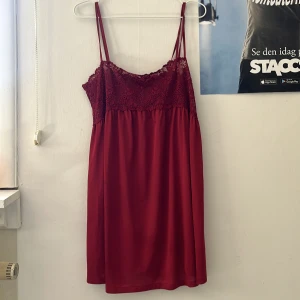 Vinröd spetsklänning med smala axelband - Vinröd kortklänning med dubbla smala axelband och vacker spets upptill. Klänningen har en flowy kjol och romantisk känsla, perfekt för sommarens tillfällen. Spetsen täcker hela överdelen och ger en feminin look.