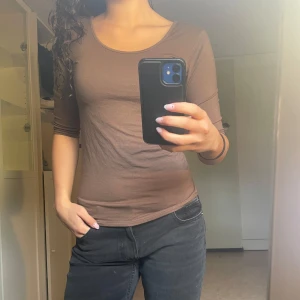 Brun långärmad topp med rund hals - Säljer en brun långärmad topp med rundad halsringning, trekvart ärmar och tight passform. Tillverkad i mjukt bomullsmaterial, perfekt för lager-på-lager eller som den är. Enkel och stilren design som passar till mycket.