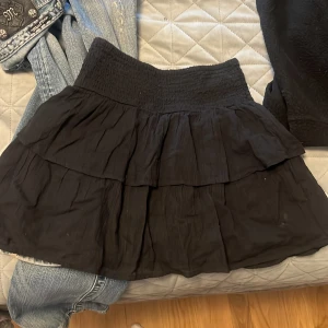 Svart lågmidjad volangkjol med resårmidja - Säljer en svart lågmidjad kortkjol med  resår i midjan och flera lager volanger. Kjolen är köpt för runt 250kr, pris kan diskuteras!