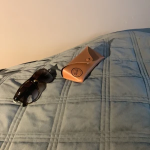 Bruna solglasögon från Ray-Ban - Snygga solglasögon från Ray-Ban med bruna bågar och mörka glas. Modellen har en klassisk, lite oversized form och kommer med ett beige fodral med Ray-Ban-logga. Perfekt accessoar för soliga dagar.