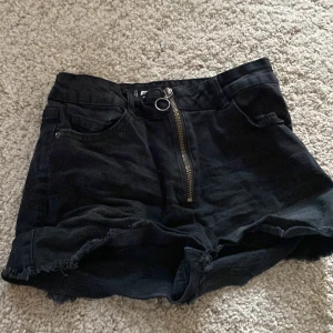 Svarta högmidjade jeansshorts från FB Sister - Svarta jeansshorts från FB Sister i högmidjad modell med råa kanter och dragkedja framtill. Klassisk femficksdesign och snygg, enkel look som passar perfekt till sommaren.