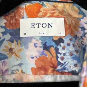 Blommig skjorta från Eton - Säljer en färgstark blommig skjorta från Eton i slim fit. Skjortan har lång ärm och ett mönster i blått, orange, lila och vitt. Perfekt för dig som vill sticka ut med en snygg och unik skjorta från ett välkänt märke.