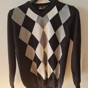 Svart och vit tröja med diamantmönster - Snygg svart tröja med ett klassiskt diamantmönster i vitt och grått på framsidan. Tröjan har en v-ringad hals och långa ärmar, perfekt för en stilren look. 100% bomull. Storlek 170. Kan hämtas i Vallentuna.