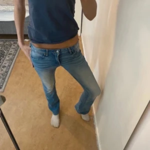 Ljusblå bootcut jeans - Säljer ett par ljusblå jeans med bootcut-modell och låg midja. Jeansen har klassisk femficksdesign, knapp- och dragkedjestängning samt lätt slitna detaljer framtill. Perfekta för en avslappnad och trendig look.