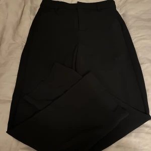 Svarta kostymbyxor - Säljer ett par klassiska svarta kostymbyxor med normal passform och raka ben. Byxorna har hällor för bälte och stängs med dragkedja och knapp och har även en hög midja . Perfekta till en stilren look.