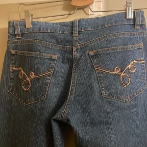 Blå flare jeans med broderade bakfickor - Blåa flare jeans med mid/ low waist. Dragkedjan åker ner därför sitter ett litet gummiband som man sätter runt jeansknappen för att hålla gylfen uppe. 