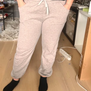 Gråa mjukisbyxor med snörning - Säljer ett par gråa mjukisbyxor med dragsko i midjan och fickor på sidorna. Säljer då dem har blivit för små. Byxorna har en avslappnad passform och är perfekta för en chill dag hemma. Mjukt material som känns skönt mot huden. Vet inte vart dem är ifrån.