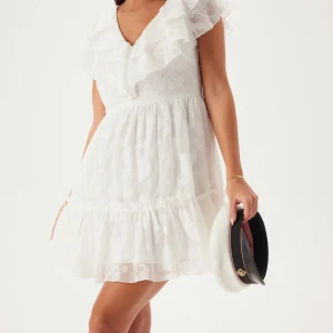 Vit volangklänning med blommönster - Superfin vit kortklänning med volangdetaljer och subtilt blommönster. Helt ny, med lappen kvar. Slutsåld på bubbleroom!