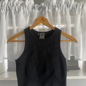 Svart ribbad linnetopp från Stronger - Säljer en svart ribbad linnetopp från Stronger. Toppen är ärmlös och har en tight passform, perfekt för träning eller som ett basplagg. Materialet är mjukt och stretchigt med 94% nylon och 6% elastan.