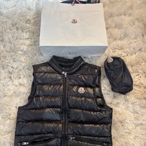 Moncler väst  - Snygg svart dunväst från Moncler med glansig finish och klassisk logotyp på bröstet.                                                   Knappt använd, är i nytt skick! Äktenhetsbevis finns också!! 