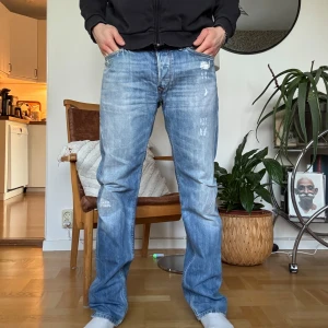 Ljusblå jeans från Diesel - Säljer ett par ljusblå jeans från Diesel med klassisk femficksdesign och raka ben. Jeansen har slitningar och en något tvättad look, samt svart läderpatch med Diesel-logga bak i midjan.