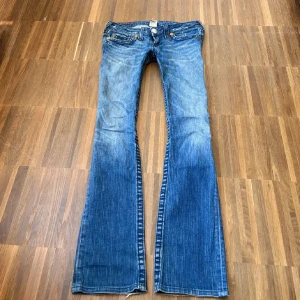 Blå bootcut jeans från True Religion - Säljer ett par klassiska blå jeans från True Religion med bootcut-passform. Jeansen har tydliga kontrastsömmar, broderade bakfickor och knappar framtill. Perfekta för dig som gillar en tidlös denimlook med extra detaljer. midja 40 innerbenslängd 81❤️ 