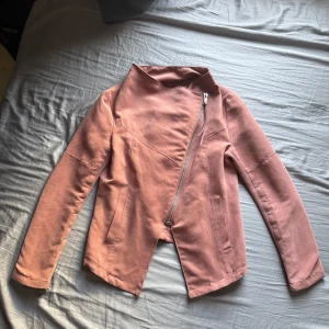 Rosa jacka med sned dragkedja från H&M Divided - Säljer en snygg rosa jacka från H&M Divided med sned dragkedja framtill. Jackan har lång ärm, två fickor och en modern, lite kortare passform baktill. Den har endast använts ett par gånger.
