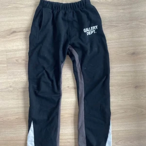 Svarta mjukisbyxor från Gallery Dept. - Säljer ett par svarta mjukisbyxor från Gallery Dept. med elastisk midja och vita samt grå detaljer längs benen. Byxorna har en avslappnad passform och är perfekta för en bekväm stil. Använd ett fåtal gånger. Öppningen längst ner vid fötterna är rätt så vidga så de dessa är super snygga! Rätt långa passar 185+