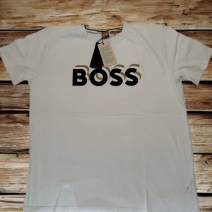 🔥Helt Ny- Exklusiv BOSS T-shirt – 100% bomull med UV-skydd! 👕 - Uppdatera din garderob med denna stilrena och tidlösa T-shirt från ikoniska BOSS! Perfekt för dig som vill ha både komfort, kvalitet och ett modernt uttryck i vardagen. Produktinformation: 	•	Märke: BOSS (Hugo Boss) 	•	Modell: Vit T-shirt med tydlig BOSS-logga 	•	Material: 100% bomull – mjuk, hudvänlig och slitstark 	•	UV-skydd: Behandlad för att ge utmärkt skydd mot solens skadliga strålar (UPF 40+), vilket blockerar minst 97,5% av UV-strålningen 	•	Passform: Regular fit – passar de flesta. 