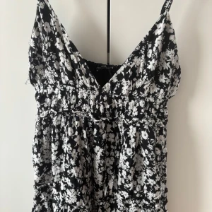 Svartvit blommig klänning från Bershka - Supersöt svart klänning med vita blommor. Klänningen har v-ringning och är från Bershka. Jättefin och använd fåtal gånger. När jag har på mig den så går den cirka 15 cm över mina knän. Jag är 165.