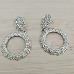 Silvriga glittriga cirkelörhängen - Snygga örhängen i silverfärg med glittrig yta och rund, öppen design. Örhängena har en texturerad, nästan bubblig kant och sitter med klassisk stiftbaksida. Perfekta för att ge din look lite extra bling och cool vibe.