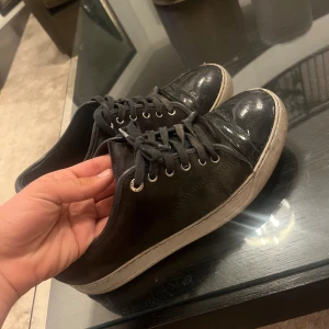 Lanvins  - Säljer ett par svarta sneakers med vit sula och svarta skosnören. Skorna har rund tå och platt sula, perfekt för en avslappnad stil. Passar till jeans eller andra vardagskläder.
