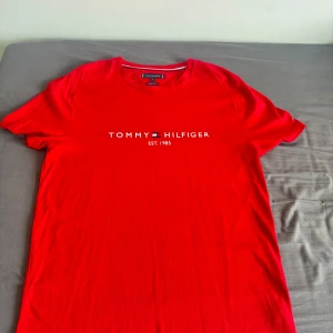 Röd Tommy Hilfiger t-shirt XL - Snygg röd t-shirt från Tommy Hilfiger i ekologisk bomull. Klassisk passform med rund hals och korta ärmar. Framsidan har stilren logotyp och texten 'Est. 1985'. Perfekt för dig som gillar streetwear och vill sticka ut med en ikonisk look. Funkar även för personer med storlek L