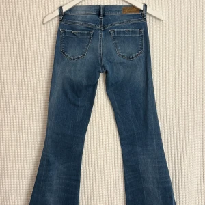 Blå bootcut jeans från Diesel - Snygga blå bootcut jeans från Diesel med klassisk femficksdesign och råa, fransiga benslut. Jeansen har en normal passform och är tillverkade i mjukt denimtyg. Perfekta för dig som gillar en avslappnad men trendig look. jeansen har clippt för att förkorta till ~L30