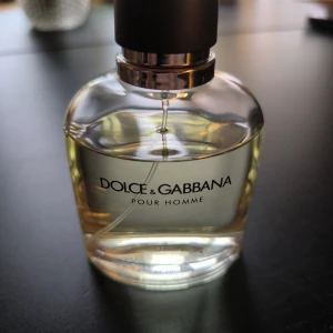 Dolce & Gabbana Pour Homme EdT 125ml - Klassisk herrparfym från Dolce & Gabbana, Pour Homme Eau de Toilette i en stilren, rundad glasflaska med svart lock och silverdetaljer. Innehåller från början 125 ml fräsch, transparent doftvätska. Perfekt för dig som gillar eleganta och tidlösa dofter. Du får avgöra mängd efter bilderna.
