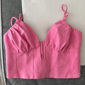 Rosa korsettopp från Zara XS - Supersöt rosa korsettopp från Zara med justerbara tunna axelband och snygga rynkade detaljer både fram och bak. Toppen har en markerad byst, croppad passform och dragkedja i sidan. Perfekt att styla med jeans, linnebyxor eller kjol för en trendig look💕