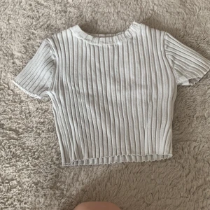 Vit ribbad topp från H&M - Superfin vit ribbad topp från H&M med korta ärmar och croppad passform. Toppen har en rund halsringning och är gjord i mjuk bomull, perfekt till jeans eller kjol. Enkel men ändå trendig med sina tydliga ribbade ränder.