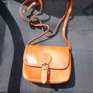 Brun axelväska i skinn från Vera Pelle - Snygg brun axelväska i äkta skinn från Vera Pelle, tillverkad i Italien. Klassisk design med justerbar rem, spänne framtill och präglad logga. Insidan har ett fack med dragkedja för småprylar. Perfekt storlek för mobilen och det viktigaste.