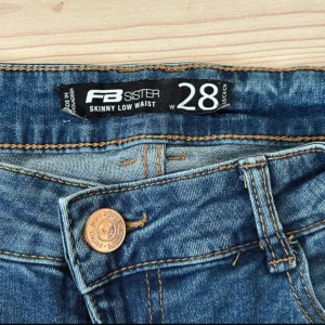 Blå skinny jeans från FB Sister - Snygga blå skinny jeans från FB Sister med låg midja. Jeansen har slitna detaljer vid knäna och fransade benslut för en trendig look. Klassisk femficksmodell med dragkedja och knapp. Perfekta för dig som gillar en tight passform och streetstyle.