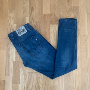 Blå Replay Anbass jeans herr - Snygga blå Replay Anbass jeans med klassisk femficksdesign och diskret logga på bakfickan. Jeansen har en tapered passform och är tillverkade i mjukt bomullsjeansmaterial. Perfekta för dig som gillar en modern men avslappnad stil.
