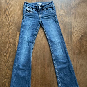 Blå bootcut jeans från Gina Tricot - Snygga blå jeans från Gina Tricot i bootcut-modell. Klassisk femficksdesign med coola ficklock bak och kontrastsömmar. Jeansen har normal passform och är tillverkade i mjukt denimtyg. Perfekta för en trendig vardagslook.