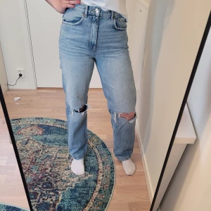 Ljusblå ripped jeans från Gina Tricot - Säljer ett par ljusblå jeans från Gina Tricot perfect jeans i modell med hög midja och raka ben.