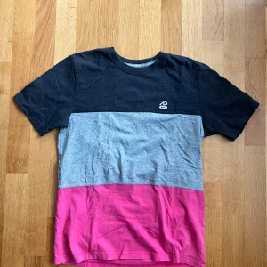 Nike ACG t-shirt i blockfärger M - Snygg t-shirt från Nike Athletic Dept. i blockfärger: svart upptill, grått i mitten och rosa nedtill. Klassisk rund halsringning och korta ärmar. Perfekt för en sportig och avslappnad stil. Tillverkad i mjuk bomull för skön känsla hela dagen.