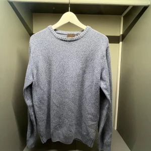 Blå stickad tröja från Oscar Jacobson - Snygg blå stickad tröja från Oscar Jacobson, tillverkad i Italien. Tröjan har rund halsringning, ribbade muddar och en klassisk passform. Perfekt för dig som gillar stilrena och bekväma plagg med en tidlös vibe.