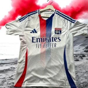 Olympique Lyonnais Adidas fotbollströja S - (Kom privat innan köp)Snygg Olympique Lyonnais matchtröja från Adidas i slim fit. Tröjan är vit med vertikala ränder i rött och blått framtill, blå Adidas-ränder på axlarna och klubbmärke på bröstet. Tillverkad i lätt och ventilerande polyester med AEROREADY-teknologi.