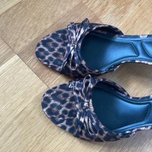 Leopardmönstrade klackar från Primark - Snygga klackar från Primark med leopardmönster i bruna och svarta toner. Skorna har öppen tå, smal hög klack och en söt rosettdetalj framtill. Perfekta för dig som vill sticka ut med ett djurmönstrat statement. Använda en gång!