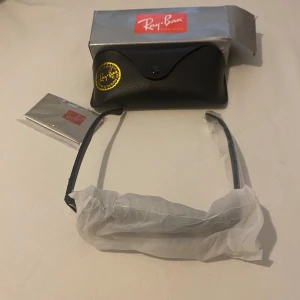 Svarta Ray-Ban Wayfarer solglasögon - Snygga svarta Ray-Ban Wayfarer solglasögon med polariserade glas. Klassisk fyrkantig form och diskret logga på linsen. Kommer med original svart fodral, putsduk och box. Perfekta för att lyfta din stil i solen.