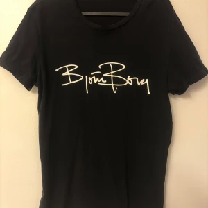 Svart Björn Borg t-shirt med tryck - Svart t-shirt från Björn Borg med vit logga i snyggt tryck över bröstet. Klassisk rund halsringning och korta ärmar. Skön passform och stilren design som funkar till det mesta. Perfekt för dig som gillar enkel men trendig stil.