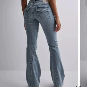 Ljusblå bootcut jeans True Religion - Snygga ljusblå jeans med bootcut-modell och markerade bakfickor med lock och knapp. Klassisk femficksdesign och hög midja. Perfekta för en trendig och avslappnad look.