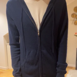 Mörkblå cashmere hoodie John Henric - Mysig mörkblå hoodie från John Henric i lyxig kashmir. Tröjan har dragkedja framtill, huva med snörning och två fickor. Perfekt för dig som vill ha en stilren och bekväm look med premiumkänsla.