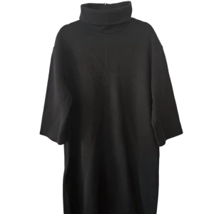 Svart stickad poloklänning - En svart stickad klänning med hög polokrage och trekvartsärmar. Modellen är loose fit och har en enkel, stilren design som passar perfekt för kyligare dagar. Klänningen är mjuk och bekväm med en rak siluett.
