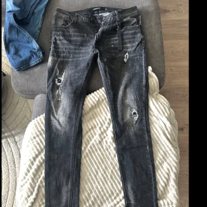 Svarta jeans från Alessandro Zavetti - Säljer ett par svarta jeans från Alessandro Zavetti i storlek 34. Jeansen har slitna detaljer framtill och coola färgstänk baktill. De är raka i modellen och har klassisk femficksdesign. 