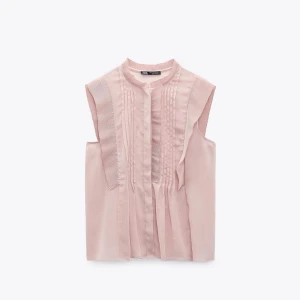 Ljusrosa ärmlös blus från Zara - Supersöt ljusrosa blus från Zara med fina veckade detaljer framtill och ståkrage. Blusen är ärmlös och har en luftig, lätt A-linjeformad passning. Perfekt för dig som gillar en stilren look. Ingår ej frakt 