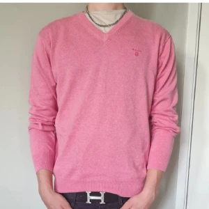 Rosa v-ringad tröja från Gant - Snygg rosa v-ringad tröja från Gant med broderad logga på bröstet. Tröjan är långärmad och har ribbade muddar vid ärmslut och nederkant. Perfekt på golfbanan likväl som på sommarfesten. Mycket gott skick, inga hål eller fläckar
