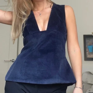 Mörkblå manchester linnetopp - Supersnygg mörkblå linnetopp i manchester med djup v-ringning och figurnära passform upptill som släpper ut nertill. Ärmlös modell som ger en cool och modern look. Perfekt att styla med både jeans och kjol för en trendig outfit.